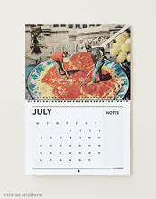 Load image into Gallery viewer, A calendar page from July hanging against a light neutral wall. The top portion shows a vintage-style art photograph of two people painting a large plate of spaghetti with tomato sauce, while the lower portion contains a black calendar grid labeled JULY and NOTES.